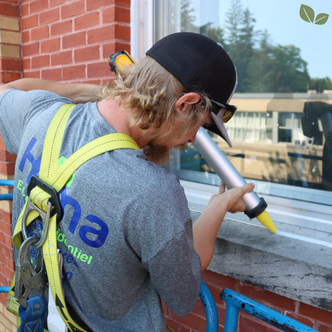Homa technician applying exterior window caulking to seal and protect a commercial building