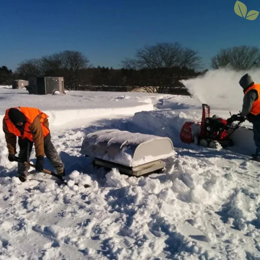 Commercial roof snow removal crew clearing snow around rooftop equipment using shovels and a snow blower