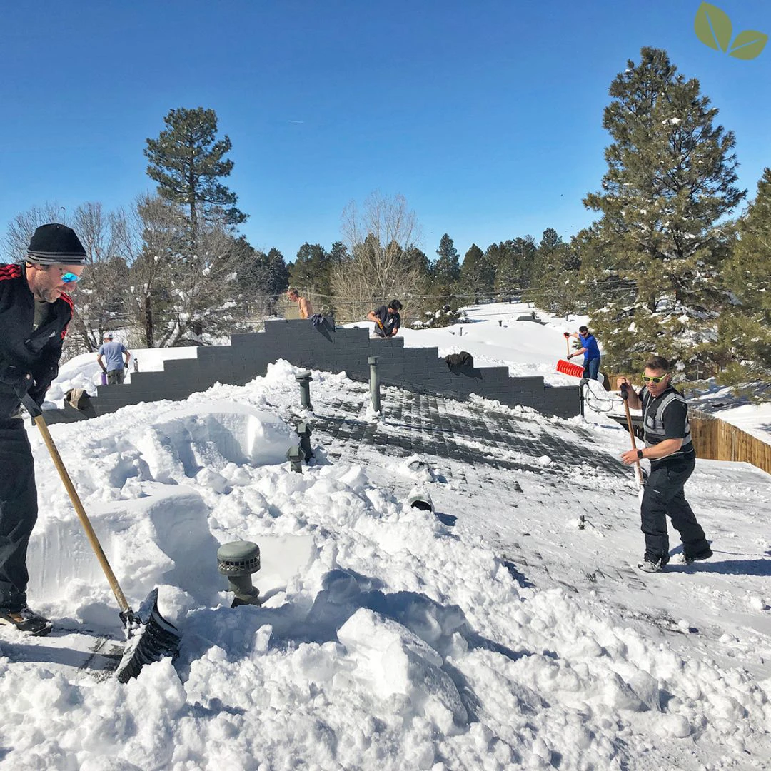 Crew manually removing heavy snow from a flat commercial roof to reduce structural load and protect rooftop systems