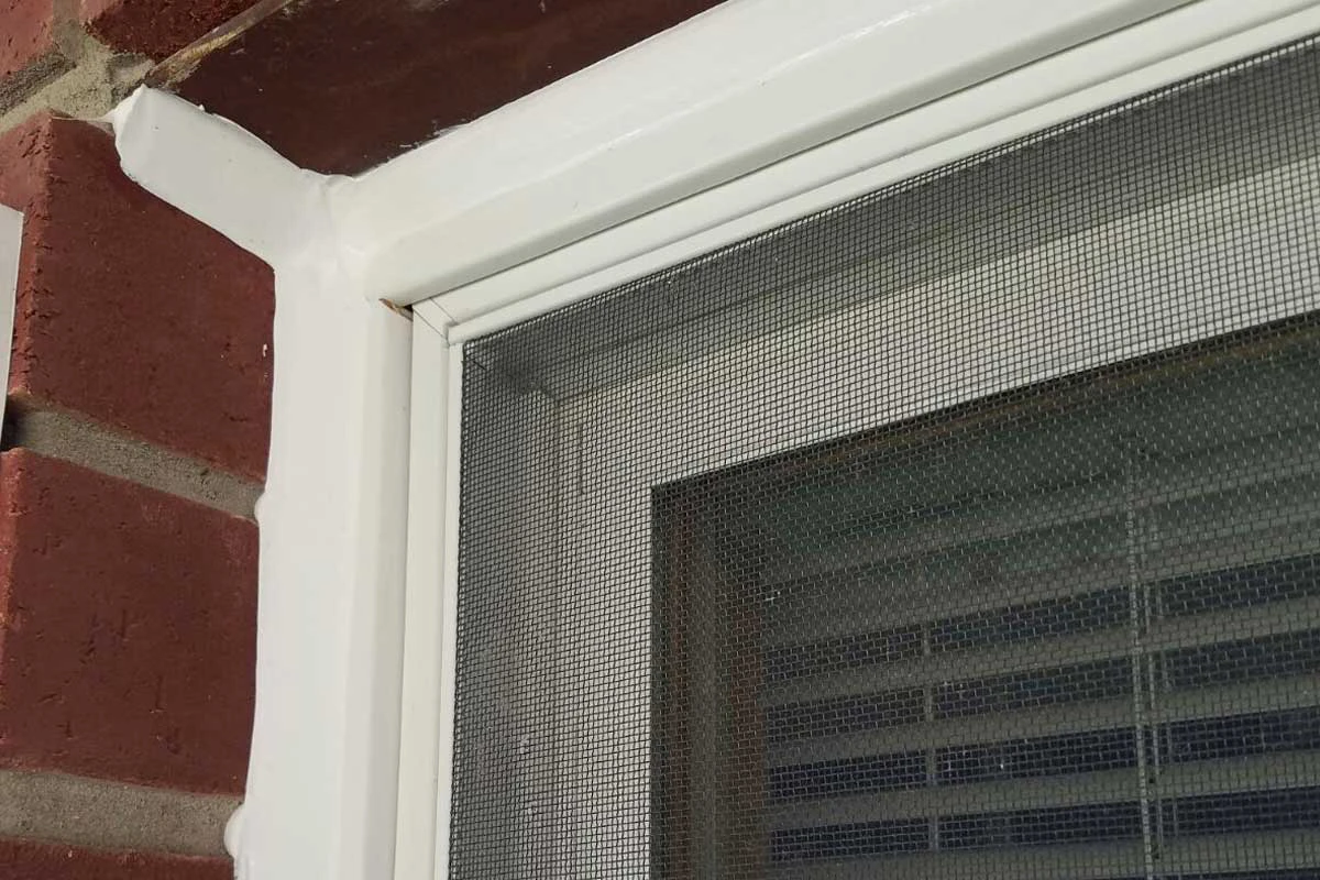 Close-up of freshly applied exterior caulking sealing the edges of a window frame on a brick wall.