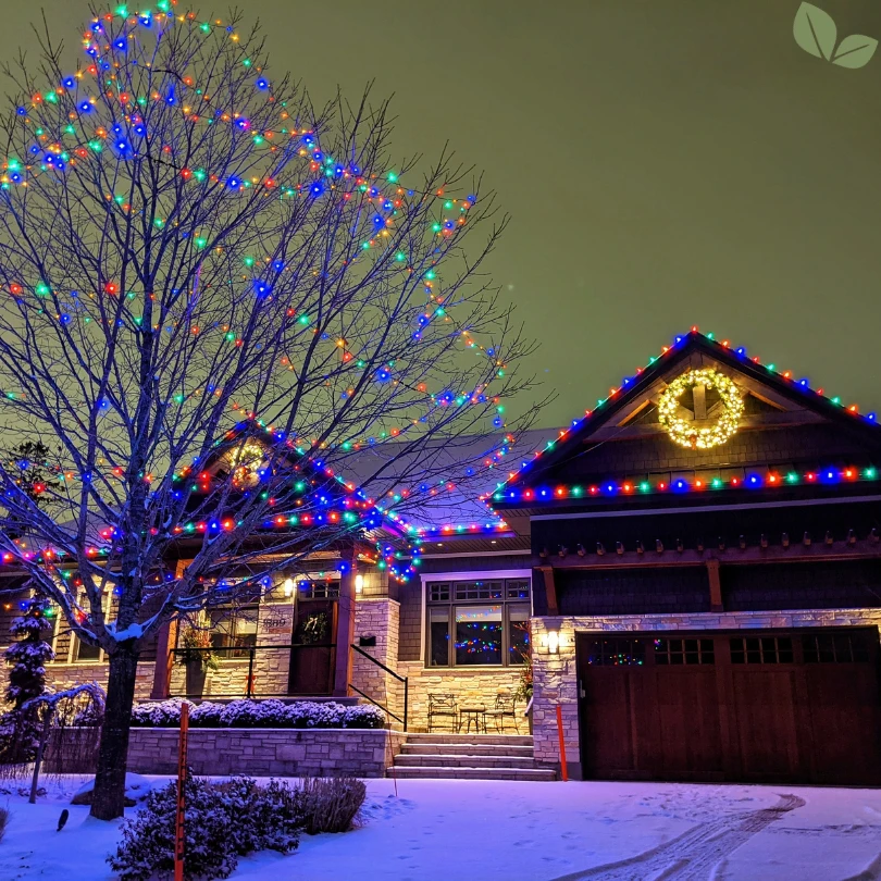 Home decorated with colorful Christmas lights on roofline and tree at night