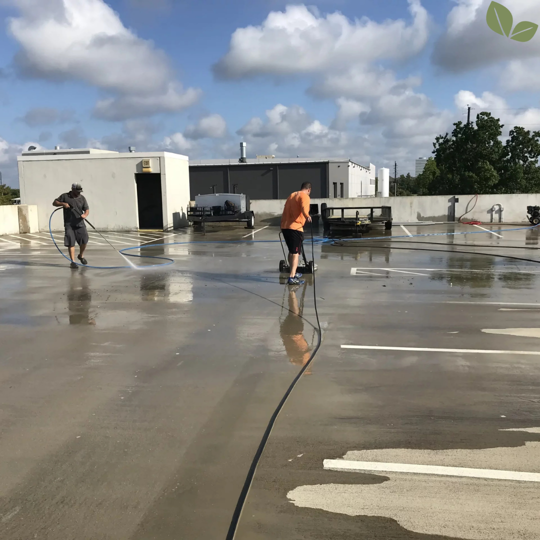 Workers pressure washing parking garage surface removing dirt and stains