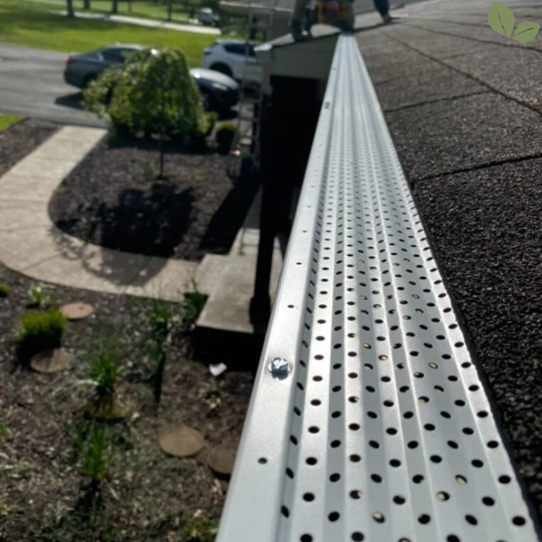 Technician installing metal gutter guard along residential roof edge